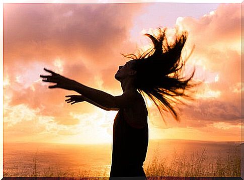 Woman with arms up and hair down at sunset